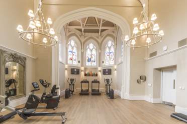 Gym at Audley Binswood Gym equipment in high, bright room with stained glass windows